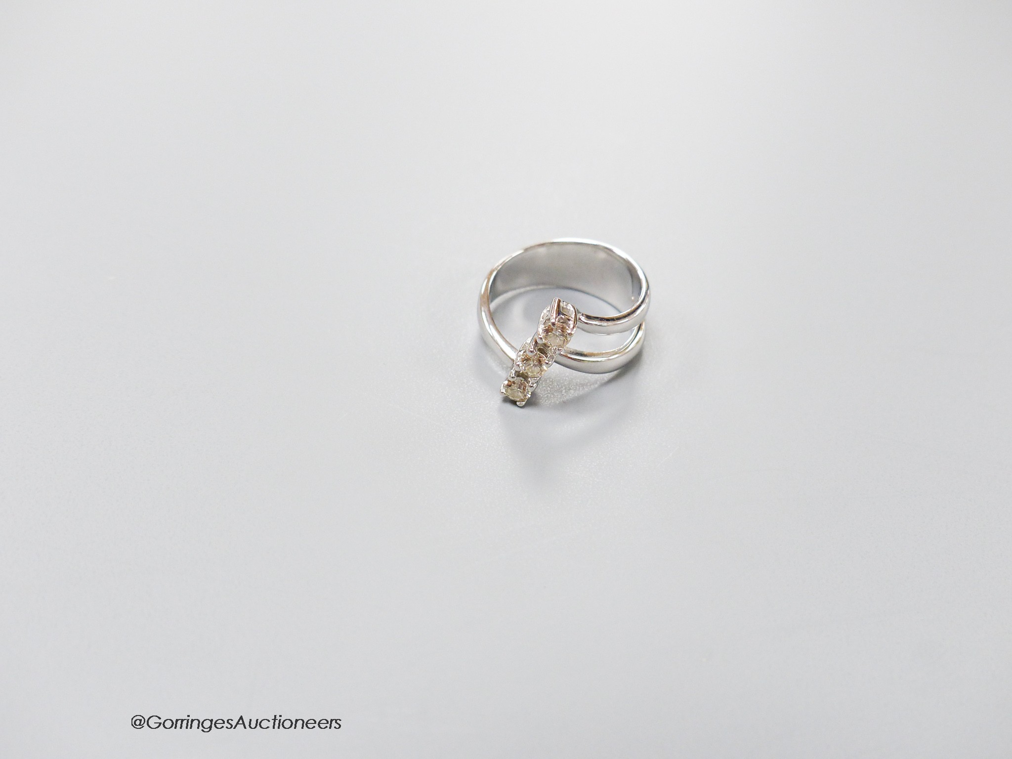 A modern white metal and three stone diamond set twin shank modernist ring, size K, gross weight 5.4 grams, with original receipt.